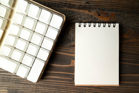 Closeup view of a computer keyboard with an empty notebook on a wooden background. Empty notebook for copy spaceの写真素材