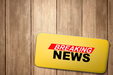 Closeup view of the mobile phone screen with breaking news inscription on a wooden background. Live broadcasting, news, and journalism conceptの写真素材