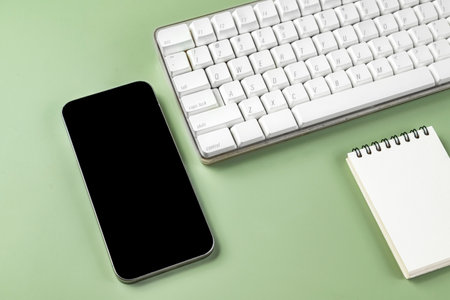 Closeup view of keyboard computer and mobile phone with blank screen and an empty notebook on a colored background. Blank mobile phone screen and empty notebook for copy spaceの写真素材