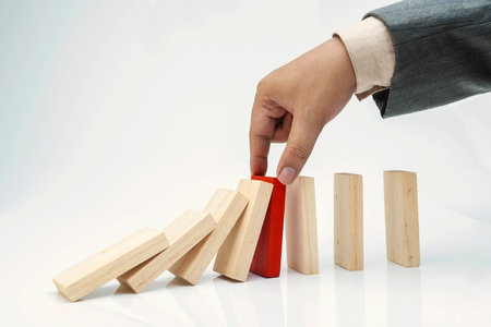 Business hand put a red wooden block into a fallen row of brown wooden blocks isolated over a white backgroundの写真素材