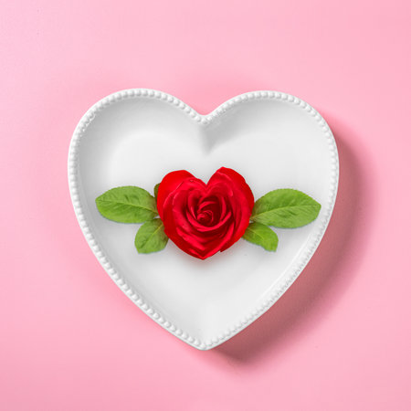 Heart plate with red rose flowerhead over a pink background. Romantic dinner Valentine's Day conceptの写真素材