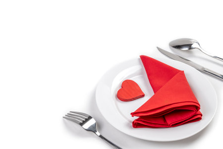 White plate with silverware of fork, knife, and spoon with red heart and red napkin isolated over white background. Romantic dinner Valentine's Day conceptの写真素材