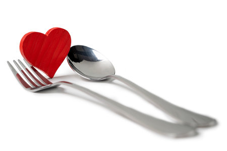 Silverware of fork and spoon with a red heart isolated over white background. Romantic dinner Valentine's Day conceptの写真素材