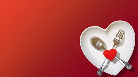 Heart plate with silverware of spoon and fork with a red heart over a red background. Romantic dinner Valentine's Day conceptの写真素材