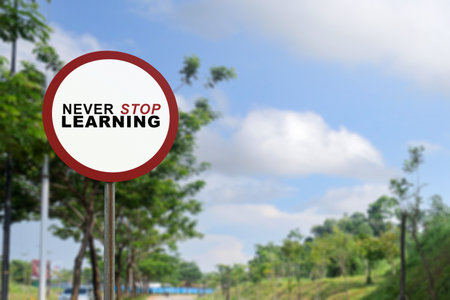 White traffic sign with text never stop learning and blue sky background. Continuous learning conceptの写真素材