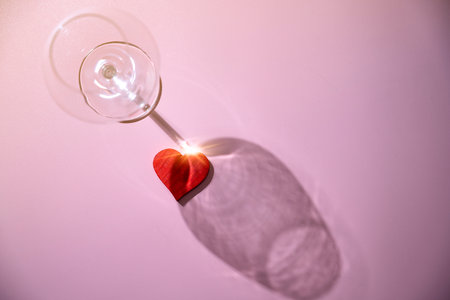 Wine glass with a red heart over a pink background. Romantic dinner Valentine's Day conceptの写真素材