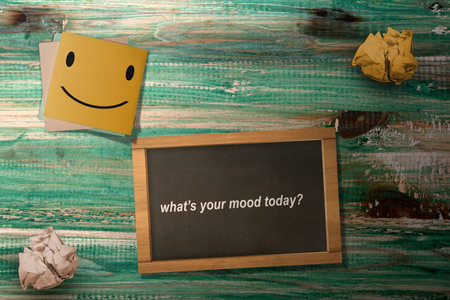 A stack of paper with a smile symbol and a small chalkboard with a 'What's your mood today' text on...
