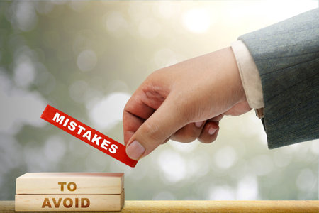 Business hand put a stack of wooden blocks with 'mistakes to avoid' text on the table. Mistake conceptの写真素材