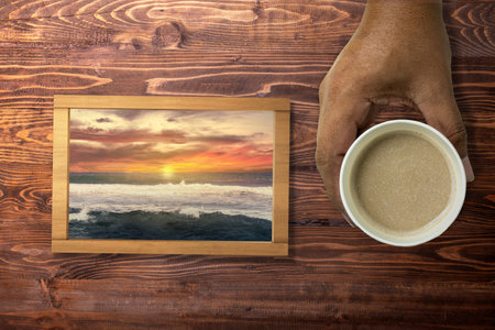 A human hand holding a cup of coffee and a small chalkboard with a nature view on the table. Health mindfulness conceptの写真素材