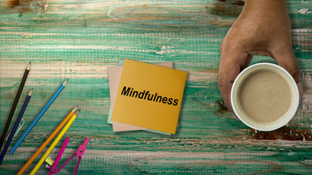 A human hand holding a cup of coffee with a stack of paper with mindfulness text on the table. Health mindfulness conceptの写真素材