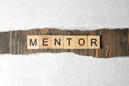 Ripped paper with a row of wooden cubes with 'mentor' text on a wooden background. Mentorship...
