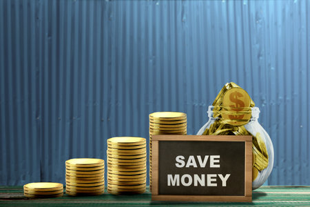 Stair stack of golden coins and golden coins inside the jar with a small chalkboard with 'save money' text on the table. Saving money conceptの写真素材