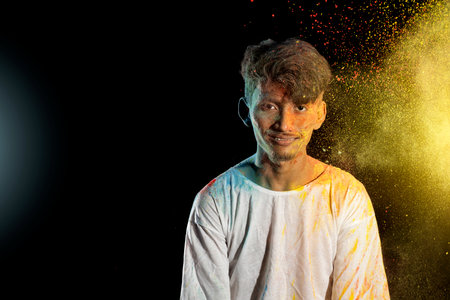 Asian man splashed with colorful holi powder and having fun isolated on black background. Color...