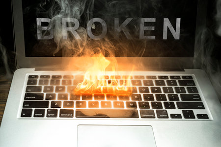 Close up laptop burned with flame and smokes on a wooden desk with broken word isolated over black background. Broken equipment.の写真素材