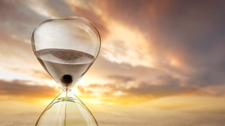 Flowing sand in the hourglass with a dramatic sky background. Time passing concept