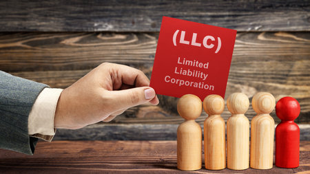 Business hand holding a note with LLC text, the acronym of Limited Liability Company with a row of wooden peg dolls on the table. Business conceptの写真素材