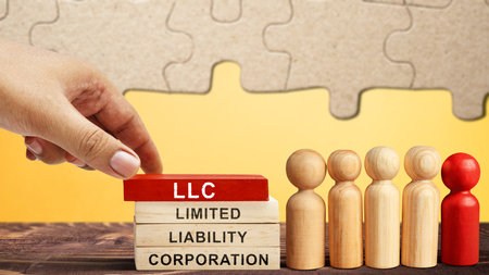 Business hand put a stack of wooden blocks with LLC text, the acronym of Limited Liability Company with a row of wooden peg dolls on the table. Business conceptの写真素材