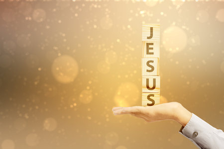 A human hand holding a stack of a cube with the text of Jesus with a blurred light background. Christian conceptの写真素材