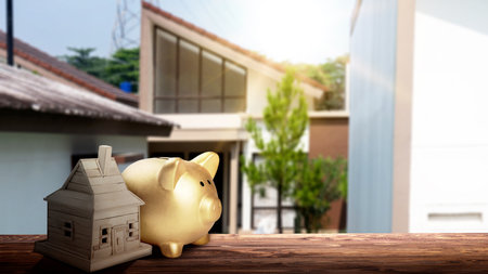 Piggy bank and a wooden house on the table with a real estate background. Real estate sales conceptの写真素材