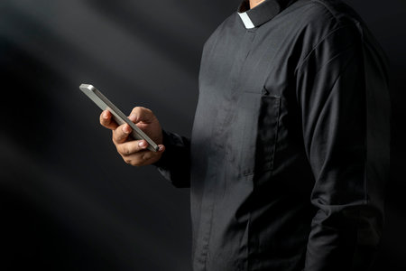 Portrait of a pastor using a mobile phone on a black background. Christian concept