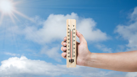 Human hand holding thermometer with hot temperature with a sky background. Environment, global...