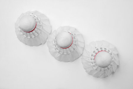 Three white badminton shuttlecocks with red details arranged neatly on a white surface, creating a...