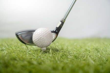 Closeup view of a golf ball on a tee with a driver club positioned for the swing, with a focus on the texture of the golf ball against a blurred natural backgroundの写真素材