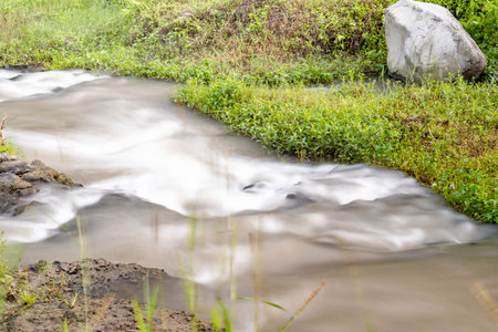 A river with a rock in it. The water is flowing and the grass is green in Grojogan Watu Purbo,...