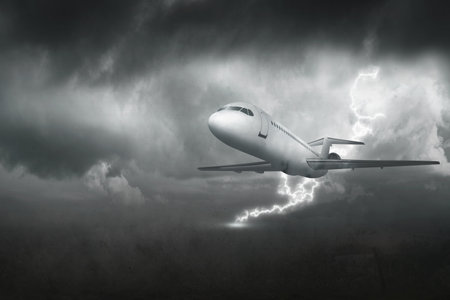 A white airplane flying through a stormy sky. The sky is dark and cloudy, and there is a lightning bolt in the air. Scene is tense and dramatic, as the airplane is flying through a dangerousの写真素材