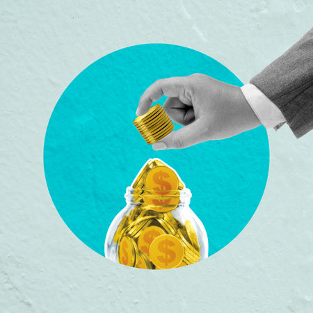 Male hand putting coins in a glass jar full of golden coins on a blue background. Concept of business, investment, finance, and passive incomeの写真素材