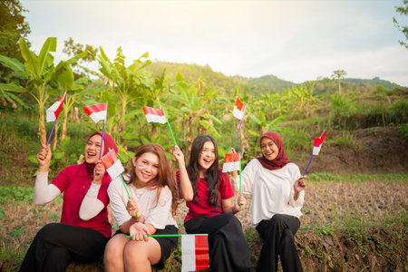 Portrait group of women with excited expressions holding small Indonesian flag outdoors with sunrise sky backgroundの写真素材