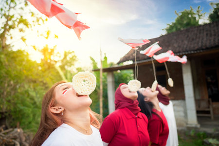 A group of women are eating creakers contest. The flags are red and white. The women are smiling and enjoying themselves. Indonesian independence conceptの写真素材