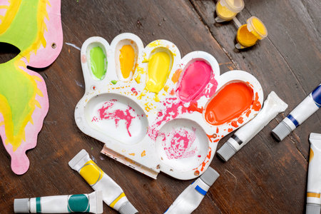 A palette with paint on it and a bunch of tubes of paint next to it. The palette is full of...