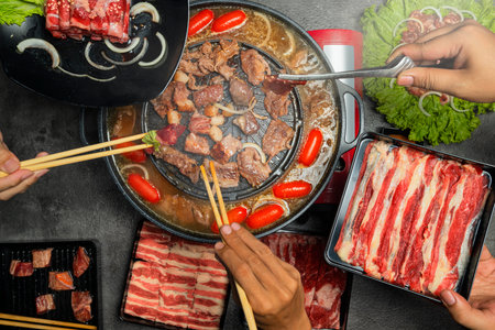 A group of people are eating meat, including beef, pork, and chicken. They are using chopsticks to eat the foodの写真素材