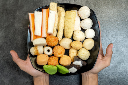 A person is holding a tray of assorted food items, including a variety of different colored balls and a few pieces of meat. The tray is placed on a countertopの写真素材