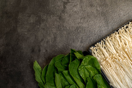A tray of white mushrooms sits next to a tray of green vegetables. The vegetables are fresh and vibrant, while the mushrooms are neatly arranged in a trayの写真素材