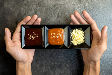 A person is holding three small black plates with different sauces. Concept of variety and choiceの写真素材