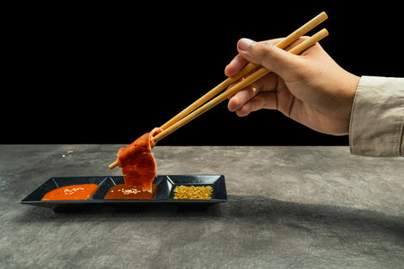 A person is eating with chopsticks and dipping food into a sauce. Concept of enjoyment and relaxation as the person savors their mealの写真素材