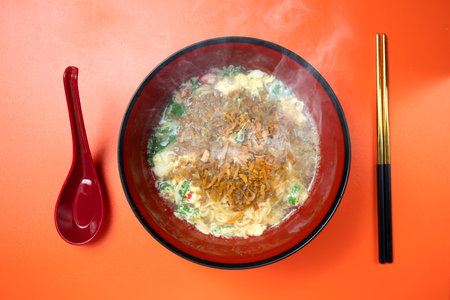 A bowl of instant noodles with a spoon next to it. The bowl is red and black and the spoon is redの写真素材