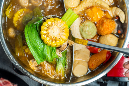 A person is scooping food out of a large pot with a spoon. The food in the pot includes corn,...