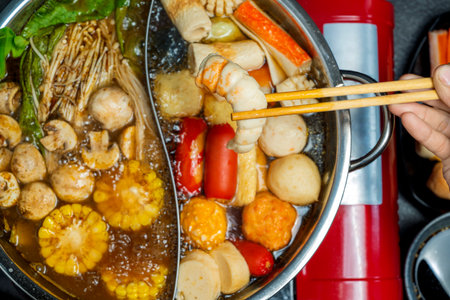 A person is eating food from a large pot of food. The food includes meat, vegetables, and seafoodの写真素材