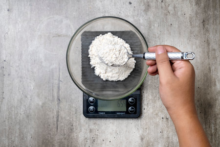 A person is measuring flour on a scale. The scale reads 664 gramsの写真素材