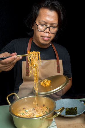 A man is eating instant noodles with chopsticks. The noodles are long and red