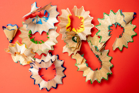 A pile of broken pencil shavings on a red background. The shavings are in various shapes and sizes, and they are scattered across the surface. Concept of messiness and disorganizationの写真素材