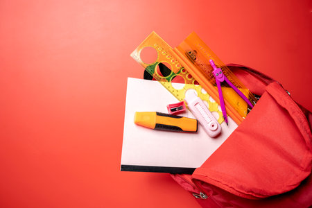 A red backpack with a white piece of paper and a red marker inside. The backpack is full of school...