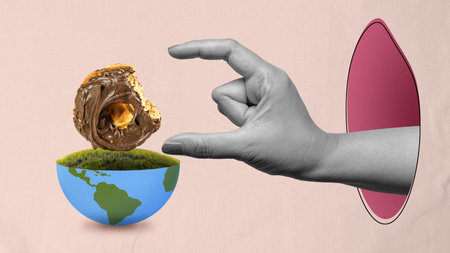 A hand is holding a chocolate mini donut in front of a bowl with a green globe. Concept of...