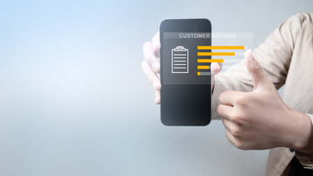 A person is holding a cell phone that has a screen displaying a list of customer ratings. Concept of customer feedback and the importance of gathering and analyzing it to improve products or servicesの写真素材