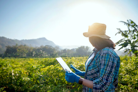 A woman wearing a blue plaid shirt and a hat is looking at a tablet. She is wearing a blue glove on her left handの写真素材