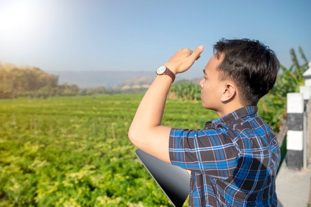 A man wearing a watch is looking at a field of green plants. The field is lush and full of life, and the man seems to be admiring itの写真素材