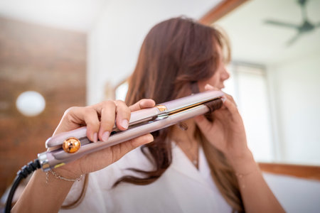 Indonesian housewife are using a hair straightener. She is holding the straightener in her hand and...